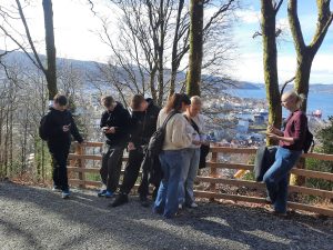 Studerende ved udsigtspunkt over Bergen i Norge med skov, fjord og panoramaudsigt til by og natur.