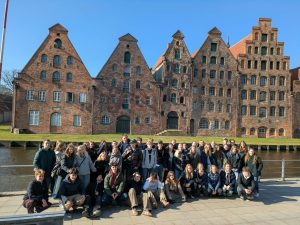 Gruppe af studerende foran historiske rødstensbygninger ved havnen i Lübeck på studietur i Tyskland.