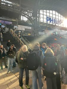 Mennesker på Hamburg Hauptbahnhof med sollys gennem stationens store glastag og fokus på transport og storbyliv.