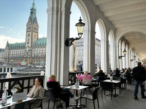 Café ved Rathausmarkt i Hamburg med udsigt til det historiske rådhus, kanaler og klassisk arkitektur i centrum.