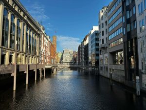 Kanal i Hamburg centrum omgivet af moderne og historiske bygninger med udsigt til broer og byliv i solskin.