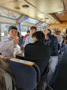 Unge studerende sidder sammen på kanalrundfart i København og nyder socialt fællesskab og sightseeing på vandet.